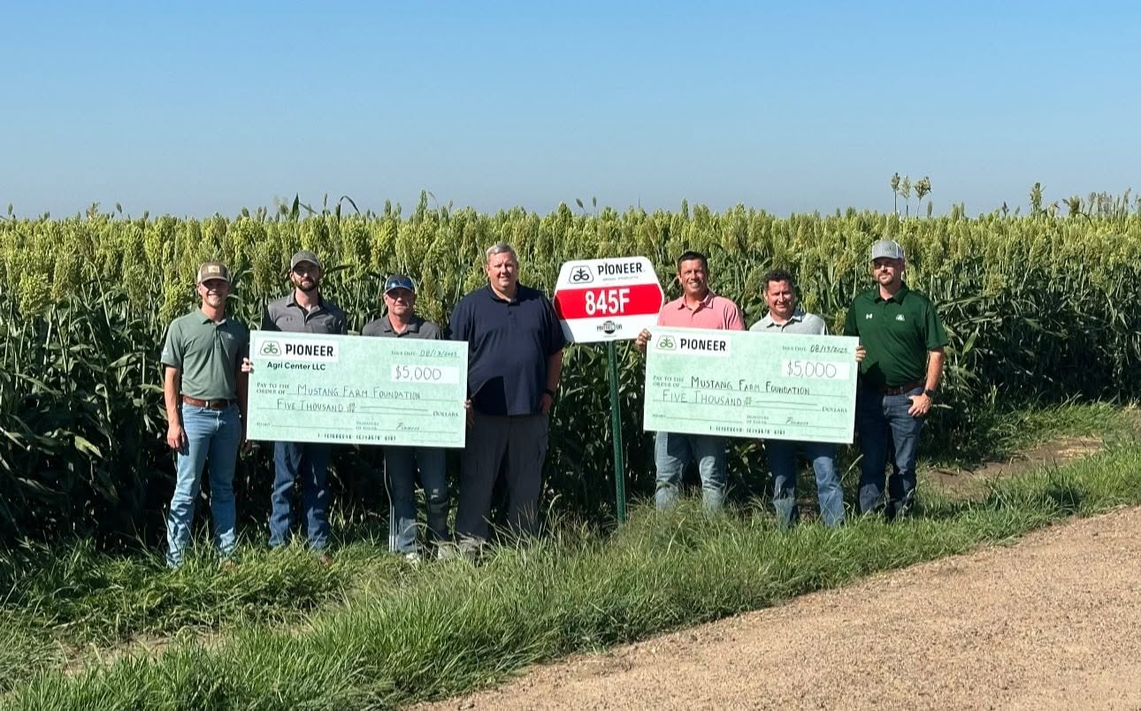 Foundation supporters holding Pioneer donation checks in a sorghum field