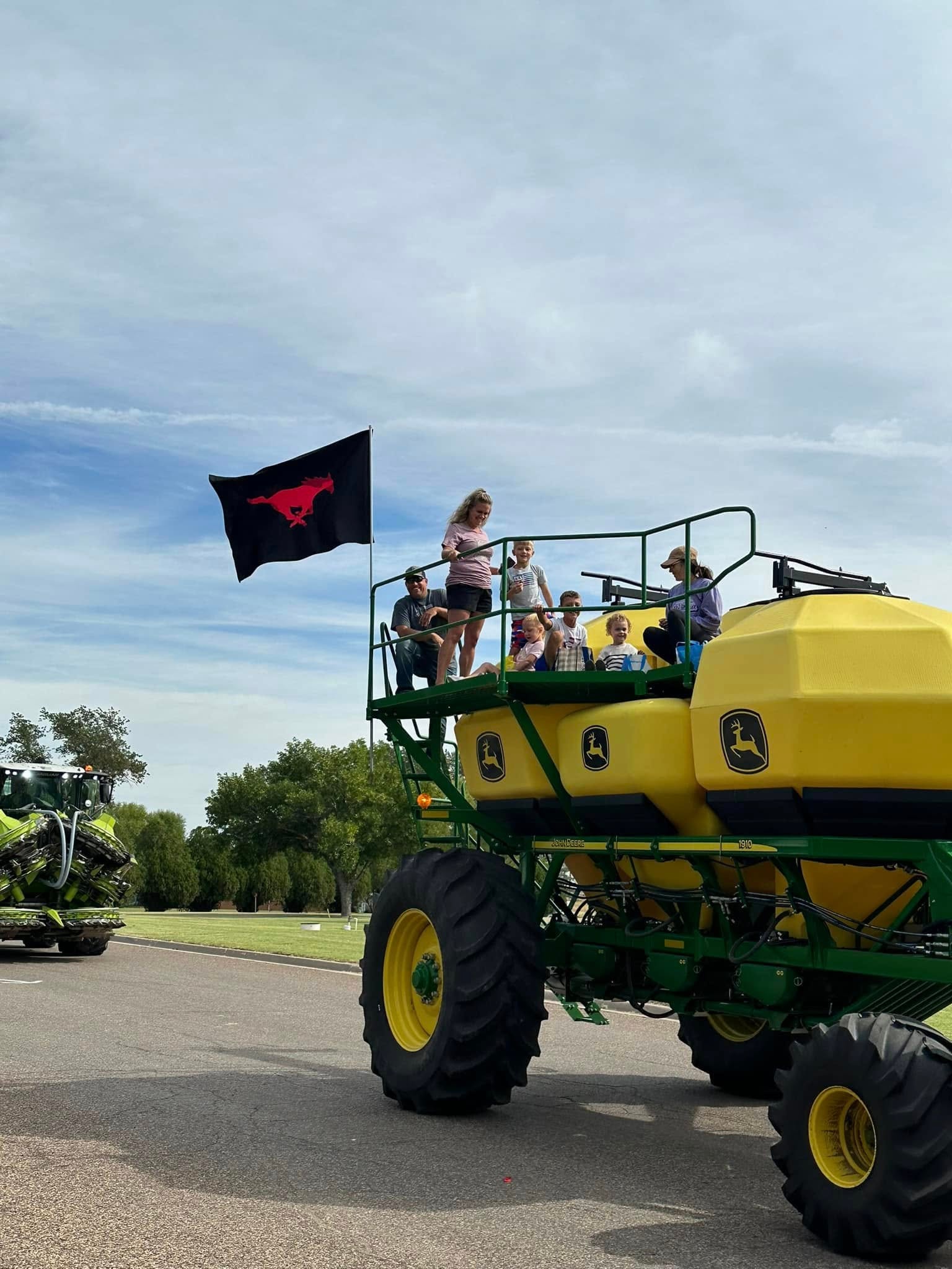 Family riding on John Deere equipment in a parade with the Mustang Farm Foundation flag